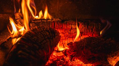 Şöminede yanan odunların samimi arka planı. Parlayan közlere ve sıcak alevlere yakın çekim. Konfor, sıcaklık ve kış kızarıklığı kavramı.