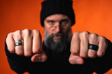 Kararlı sakallı bir adamın yumruklarına odaklanmış güçlü bir portre. Güç kavramı, yüzleşme ve turuncu arka planda protesto