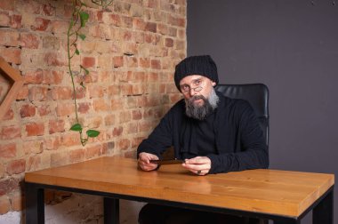 Kendine güvenen, sakallı modern bir iş adamı, çatı katında bir ofiste tuğla duvarlı bir masada oturuyor, katlanabilir bir akıllı telefon tutuyor. İş, teknoloji ve liderlik kavramı
