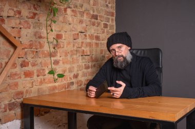 Kendine güvenen, sakallı modern bir iş adamı, çatı katında bir ofiste tuğla duvarlı bir masada oturuyor, katlanabilir bir akıllı telefon tutuyor. İş, teknoloji ve liderlik kavramı