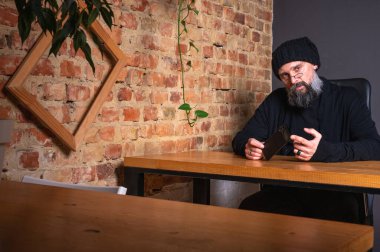 Kendine güvenen, sakallı modern bir iş adamı, çatı katında bir ofiste tuğla duvarlı bir masada oturuyor, katlanabilir bir akıllı telefon tutuyor. İş, teknoloji ve liderlik kavramı