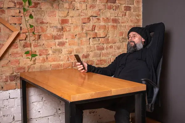 Kendine güvenen, sakallı modern bir iş adamı, çatı katında bir ofiste tuğla duvarlı bir masada oturuyor, katlanabilir bir akıllı telefon tutuyor. İş, teknoloji ve liderlik kavramı