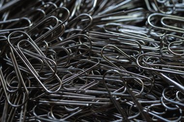 A chaotic yet captivating close-up of numerous metallic paper clips in a monochrome palette, highlighting their intricate shapes and textures. Ideal for office, creativity, and abstract themes