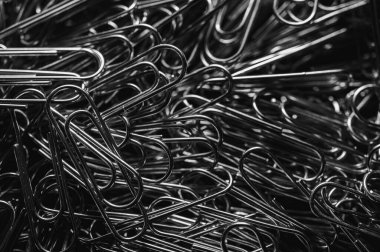 A chaotic yet captivating close-up of numerous metallic paper clips in a monochrome palette, highlighting their intricate shapes and textures. Ideal for office, creativity, and abstract themes
