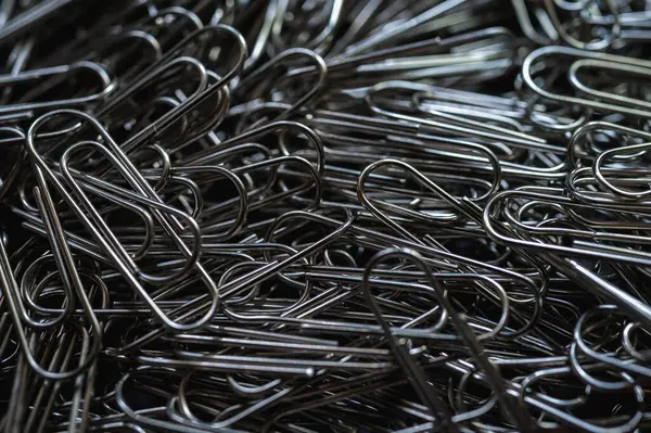 A chaotic yet captivating close-up of numerous metallic paper clips in a monochrome palette, highlighting their intricate shapes and textures. Ideal for office, creativity, and abstract themes
