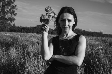 Bir tarlada siyah ve beyaz bir kadının elinde siyah ve beyaz bir fotoğraf, hatıra, melankolik ve doğal güzelliği çağrıştıran, narin gelincikler.