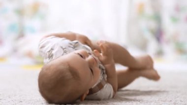 Altı aylık sağlıklı bebek, bebek odasında ilk kez sırtından karnına doğru yuvarlanarak yerde yuvarlanıyor. Çocuklarda sağlıklı büyüme ve gelişim