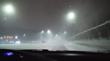 Karlı bir otoyolda gece aşırı araba kullanmak. Arabanın ön camına kar taneleri düşer..