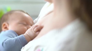 Genç bir anne yeni doğmuş bir bebeği hafif bir yatak odasında emziriyor. Annem bebeğini kucağına alıp sarılıyor. Annelik, Ebeveynlik ve Annelik. Güzel Mutlu Aile. Yakın çekim, eğim kaydırma lensi