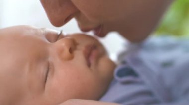 Genç ve güzel anne, uyuyan bebeğini öpüyor. Annelik, Ebeveynlik ve Annelik. Güzel Mutlu Aile. Yakın çekim, eğim kaydırma lensi.