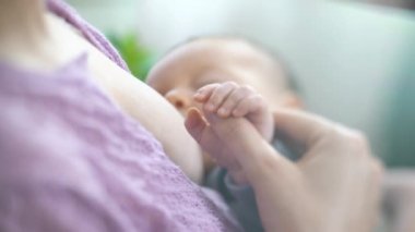 Genç bir anne yeni doğmuş bir bebeği hafif bir yatak odasında emziriyor. Annem bebeğin elini tutuyor. Korunan bebek, anne yardımcı oluyor. Güzel Mutlu Aile. Anneler Günü. Yakın çekim, eğim kaydırma lensi