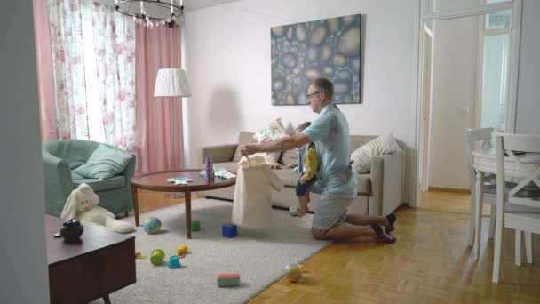 Vader Doet Schoonmaak Woonkamer Verzamelt Veel Verspreid Speelgoed Met Zijn — Stockvideo