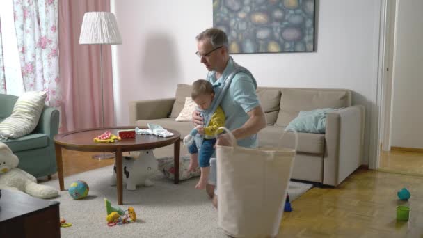 Ojciec Sprząta Salonie Zbiera Mnóstwo Rozrzuconych Zabawek Swoim Niemowlęciem Nosząc — Wideo stockowe