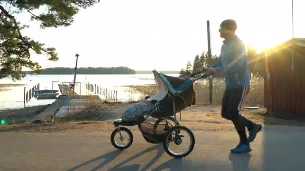 芬兰的一个夜晚 在夕阳西下的河堤上 一名男子骑着婴儿车沿着公园的一条空巷慢跑 — 图库视频影像