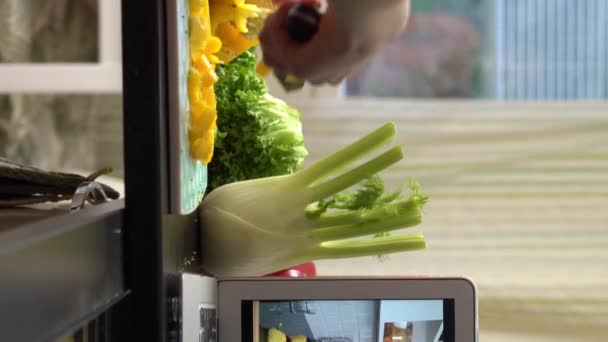 オンラインストリームビデオブログのチュートリアルを見ている若い女性おいしいと健康食品についてラップトップを使用して家庭のキッチンで食事を調理 — ストック動画