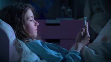 Genç kız, gece yatak odasında, akıllı telefondan mesajlaşarak sosyal medyaya kayıyor. Teknoloji, internet, iletişim ve insan konsepti. Çocuklardaki sosyal ağlara bağımlılık. Sağlıklı uyku değil.
