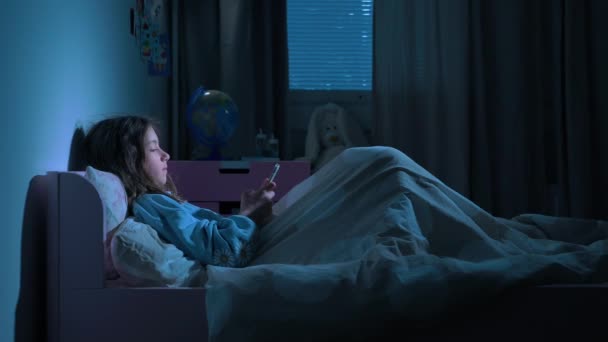 10代の女の子は スマートフォンを使用して夜にベッドに横たわって ソーシャルメディアやテキストメッセージをスクロールします 健康な睡眠じゃない 不眠症とベッドに行く前にスマートフォンの害 社会的ネットワークへの依存 — ストック動画