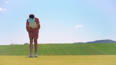 Golf oynayan olgun bir kadın. Golfçü golf topunu vuruyor ve golf deliğine vuruyor. Yeşil tepeleri ve mavi gökyüzü olan güneşli güzel bir manzara..