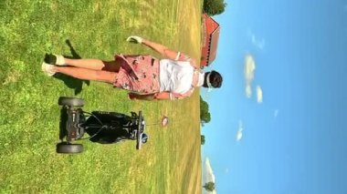 Golf oynayan olgun bir kadın. Otomatik elektrikli golf arabasıyla golf sahasında yürüyen bayan golfçü. Yeşil tepeleri ve mavi gökyüzü olan güneşli güzel bir manzara..