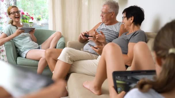 快乐的大家庭在家里一起玩网络游戏 不同年龄段的人坐在沙发上玩乐 祖父母和小女孩在客厅里用移动设备放松 — 图库视频影像
