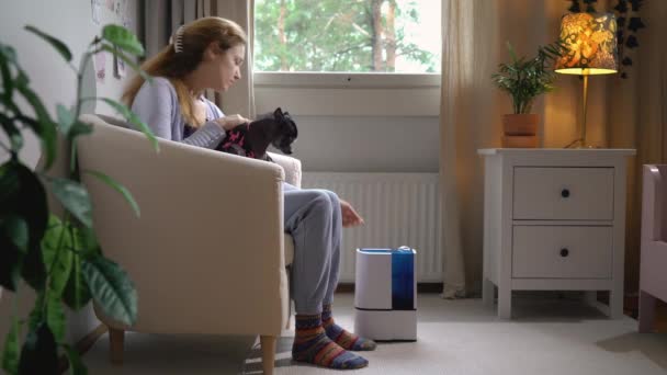 一位年轻的漂亮女子抱着一条小狗 在客厅里打开了一台现代加湿器 — 图库视频影像