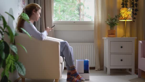 Söt Ung Kvinna Med Smartphone Slår Modern Fuktare Vardagsrummet — Stockvideo