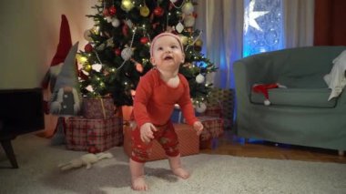 Noel arifesinde, kırmızı şapkalı mutlu çocuk bir Noel ağacının arkasında yerde sürünüyor. Mutlu tatiller, yeni yıl. Evde sıcak bir kış akşamı. Xmas zamanı.