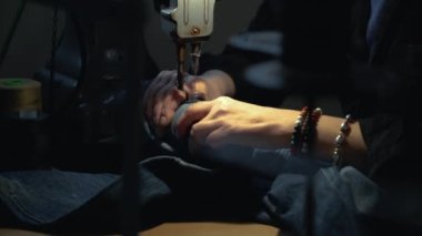 Kadın bir terzi atölyede kot giysi tamir ederken eski kotları ve eski dikiş makinesini tamir ediyor. Küçük bir aile şirketi, terzilik ve giysi tamiri, el yapımı, başlangıç. Yakın plan.