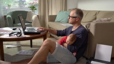 Orta yaşlı bir baba ve evde çalışan bir bebek. Yeni doğmuş bir bebeği olan bağımsız bekar bir baba video görüşmesi yapıyor ve evdeki belgelerle uğraşıyor. Uzaktan iş, çoklu görev, babalık izni ve aile.
