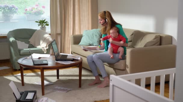 家で働く赤ちゃんと一緒にいる若い母親 新生児のフリーランスのシングルマザーがビデオ通話を行い 自宅で文書を扱っています リモートジョブ マルチタスク 出産休暇 フレーム — ストック動画