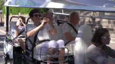 Bir grup turist Tuk-tuk elektrikli arabasıyla şehir merkezinden geçiyor. Gezginler eski kasabada çevre dostu bir araçla gezintiye çıkıyorlar.