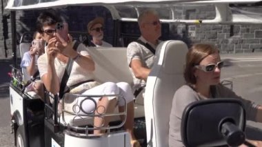 Bir grup turist Tuk-tuk elektrikli arabasıyla şehir merkezinden geçiyor. Gezginler eski kasabada çevre dostu bir araçla gezintiye çıkıyorlar.