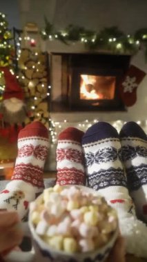 Sıcak şöminenin yanında kakaolu bir çift, Noel süsleri, Noel ağacı ve dekorasyon arka planında yün çoraplarla ayaklarını ısıtıyor. Sıcak Kış, Noel ve