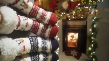 Sıcak şöminenin yanında eğlenen ve Noel süsleri, Noel ağacı ve dekorasyon arka planında yün çoraplarla ayaklarını ısıtan çift. Sıcak Kış, Noel ve Aile.