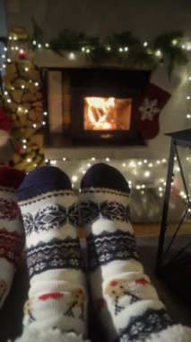 Sıcak şöminenin yanında eğlenen ve Noel süsleri, Noel ağacı ve dekorasyon arka planında yün çoraplarla ayaklarını ısıtan çift. Sıcak Kış, Noel ve Aile.