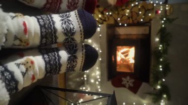 Sıcak şöminenin yanında eğlenen ve Noel süsleri, Noel ağacı ve dekorasyon arka planında yün çoraplarla ayaklarını ısıtan çift. Sıcak Kış, Noel ve Aile.