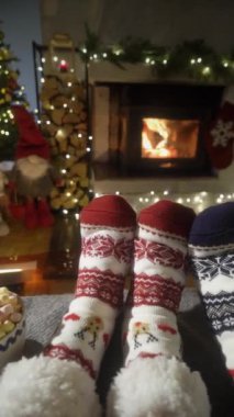Sıcak şöminenin yanında eğlenen ve Noel süsleri, Noel ağacı ve dekorasyon arka planında yün çoraplarla ayaklarını ısıtan çift. Sıcak Kış, Noel ve Aile.