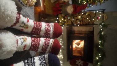 Sıcak şöminenin yanında eğlenen ve Noel süsleri, Noel ağacı ve dekorasyon arka planında yün çoraplarla ayaklarını ısıtan çift. Sıcak Kış, Noel ve Aile.
