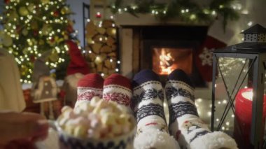 Sıcak şöminenin yanında kakaolu bir çift, Noel süsleri, Noel ağacı ve dekorasyon arka planında yün çoraplarla ayaklarını ısıtıyor. Sıcak Kış, Noel ve