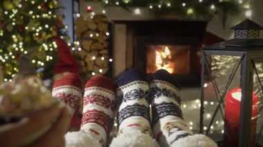 Sıcak şöminenin yanında kakaolu bir çift, Noel süsleri, Noel ağacı ve dekorasyon arka planında yün çoraplarla ayaklarını ısıtıyor. Sıcak Kış, Noel ve