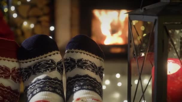 暖かい暖炉で楽しむカップルは クリスマスの装飾やクリスマスツリーや装飾の背景で盗まれた靴下で足を温めます コージーウィンター クリスマス ファミリー — ストック動画