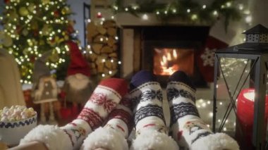 Sıcak şöminenin yanında eğlenen ve Noel süsleri, Noel ağacı ve dekorasyon arka planında yün çoraplarla ayaklarını ısıtan çift. Sıcak Kış, Noel ve Aile.