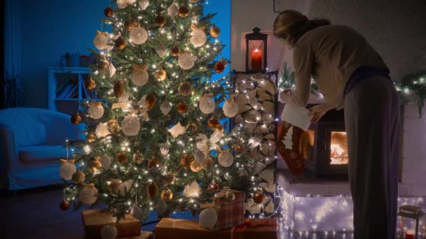 Una Mujer Decorando Árbol Navidad Acogedora Habitación Con Chimenea Decorada — Vídeo de stock