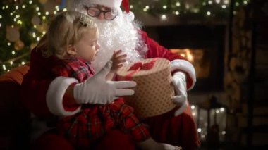 Pijamalı ve Noel Baba 'lı küçük bir çocuk Noel kurabiyelerini sütle yer ve Noel hediyelerini Noel ağacı ve şöminesi olan süslü bir oturma odasında yerleştirir.