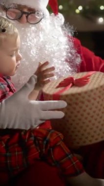 Pijamalı ve Noel Baba 'lı küçük bir çocuk Noel kurabiyelerini sütle yer ve Noel hediyelerini Noel ağacı ve şöminesi olan süslü bir oturma odasında yerleştirir.