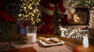 Noel Baba Noel hediyelerini şöminenin üstüne koyar, zencefilli kurabiye yer ve Noel ağacıyla süslenmiş oturma odasında süt içer.