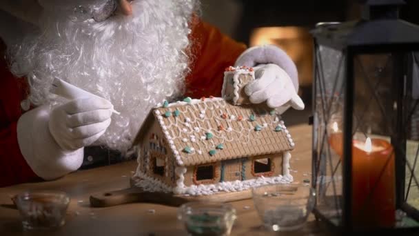 サンタクロースは暖炉とクリスマスツリーで彼の住居の甘いパターンでジンジャーブレッドハウスを飾る — ストック動画