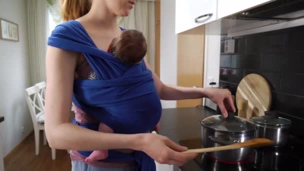 キッチンでスリング料理で寝ている赤ん坊の母親 産休中の女性 働く世帯 子供の世話をする母親の責任を楽しんでいます — ストック動画