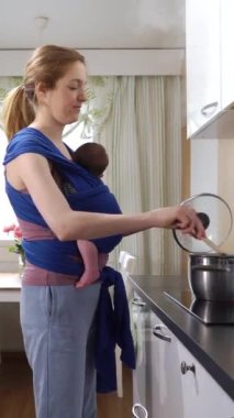 Bebeği olan genç bir anne mutfakta askı ile yemek pişiriyor. Doğum iznindeki kadın ev işlerinde çalışıyor anne annelik sorumluluğunun keyfini çıkarıyor.