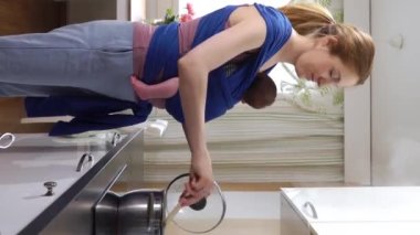 Bebeği olan genç bir anne mutfakta askı ile yemek pişiriyor. Doğum iznindeki kadın ev işlerinde çalışıyor anne annelik sorumluluğunun keyfini çıkarıyor.